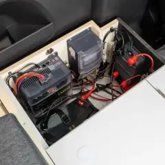 Système de batteries et de câblage pour un chauffage pour van sans électricité. L'installation est bien rangée dans un compartiment en bois.