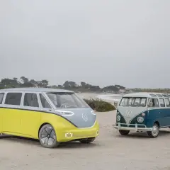 Deux combi VW, un moderne jaune et gris, l'autre vintage bleu et blanc, sur une plage brumeuse.