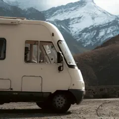 Un camping-car intégral blanc stationné sur un chemin de terre, avec des montagnes enneigées en arrière-plan.