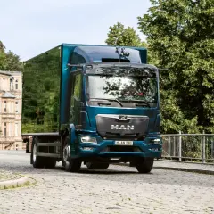 Camion MAN bleu turquoise avec remorque verte sur une route pavée.