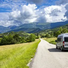 Un camping-car Elios sillonne une route sinueuse à travers les paysages verdoyants du Vercors, sous un ciel bleu parsemé de nuages.