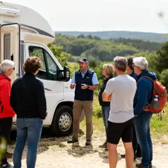 Un groupe écoute un guide près d'un camping-car, prêt pour des sorties organisées en camping-car dans un paysage verdoyant.
