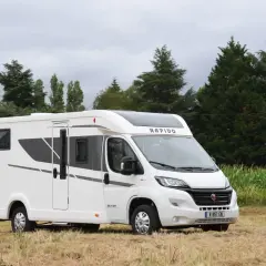 Un camping-car Rapido C86 blanc, moderne, garé dans un champ. Une jeune femme souriante se tient à droite. Avis Rapido C86.