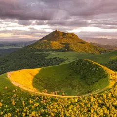 Vue panoramique du Puy de Dôme au coucher du soleil, avec un chemin serpentant sur une colline verdoyante. Idéal pour un séjour en camping-car.