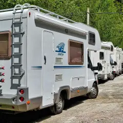 Une file de camping-cars, dont un camping car 10 mètres, stationnés sur un chemin de gravier, entourés de verdure.