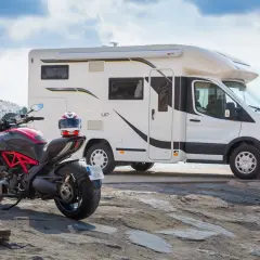 Un camping-car et une moto sportive Ducati sont garés près de la mer, prêts pour une aventure.