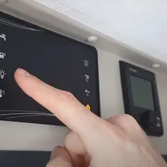 Doigt appuyant sur l'icône d'ampoule du tableau de commande cellule camping-car Challenger.