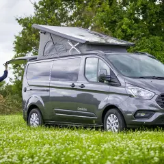 Un homme ouvre le hayon d'un van aménagé avec toilette, prêt pour l'aventure en pleine nature.
