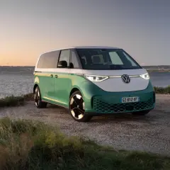Un camping-car électrique vert et blanc, prêt pour l'aventure au bord de l'eau au coucher du soleil.