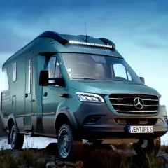 Un van tout terrain vert émeraude, prêt pour l'aventure, stationné au bord d'un lac paisible sous un ciel bleu.