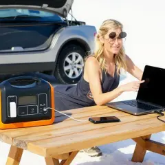 Femme travaillant sur son ordinateur portable, alimenté par un convertisseur 12 volts 220 volts camping car, près d'une voiture.