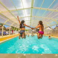 Deux filles sautent main dans la main dans une piscine couverte. Vacances en camping-car à Saint-Malo.