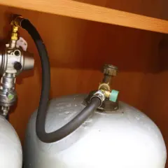 Connexion pour remplir bouteille de gaz au GPL. Tuyau noir relié à une valve verte sur la bouteille.