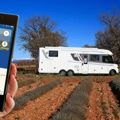 Une application camping-car à la ferme guide vers le Domaine des Oliviers. Un camping-car blanc est garé dans un champ de lavande séchée.