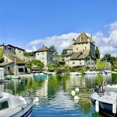 Vue d'une aire de camping-car au bord du lac Léman, avec un château médiéval, des bateaux et des maisons en pierre.
