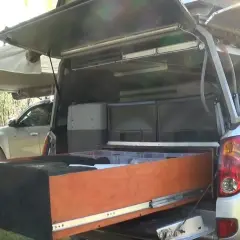 Un homme montre l'intérieur d'une cellule pick-up aménagée avec des tiroirs et des rangements, prête pour l'aventure.