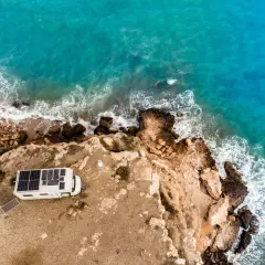 Camping-car avec panneaux solaires sur une falaise en Espagne, face à la mer turquoise. Une belle escapade de camping chez l'habitant.