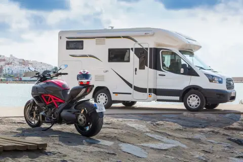 Un camping-car et une moto sportive Ducati sont garés près de la mer, prêts pour une aventure.
