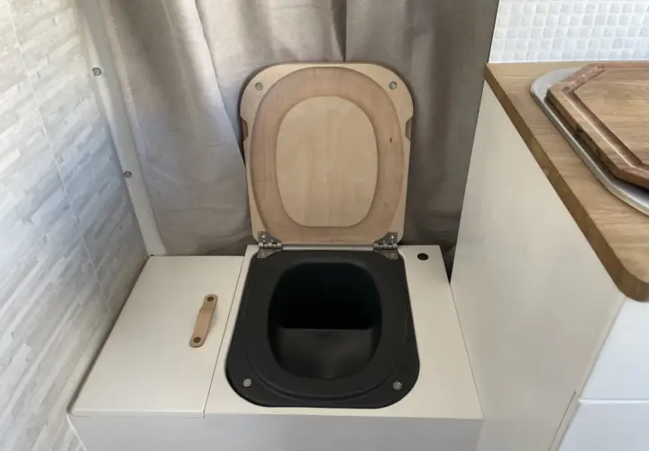 WC de camping aménagé avec abattant en bois et cuvette noire.