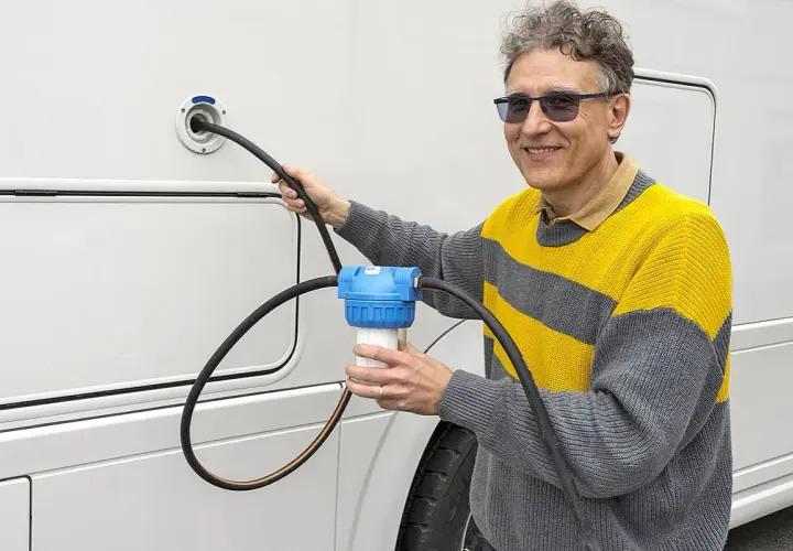 Un homme utilise un filtre à eau pour le remplissage d'eau de son camping-car. Une astuce pratique pour une eau pure en voyage.