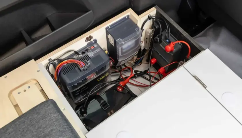 Système de batteries et de câblage pour un chauffage pour van sans électricité. L'installation est bien rangée dans un compartiment en bois.