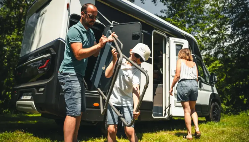 Un père et son fils sortent une chaise pliante de leur camping-car, prêts pour une aventure en Ardeche.
