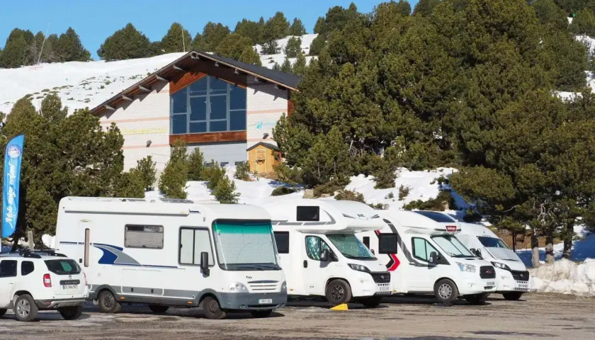 Stationnement de camping-cars dans une aire de camping car Andorre, avec un bâtiment et des pins enneigés en arrière-plan.