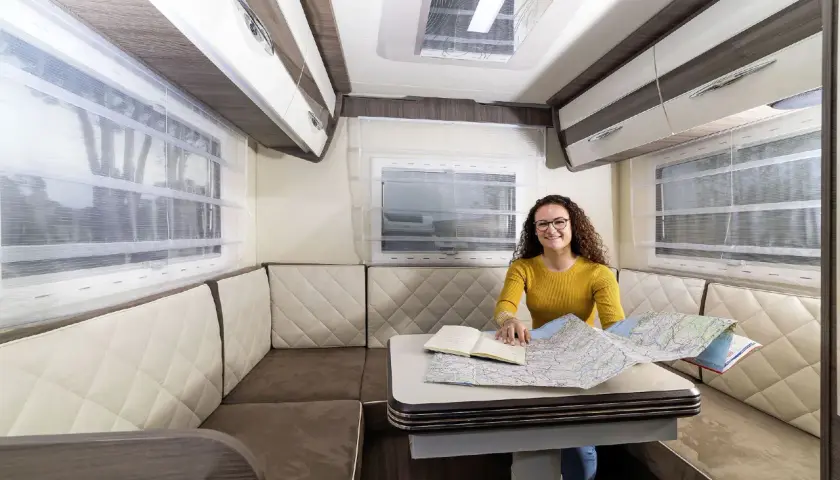 Aménagement du camping car salon arrière : une femme prépare son itinéraire sur une carte.