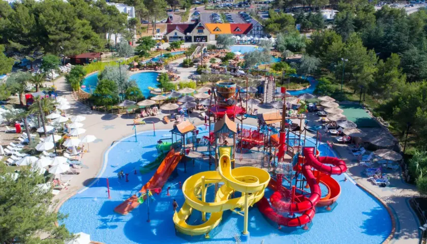 Un camping pour camping-car avec parc aquatique, offrant toboggans colorés, piscines et parasols pour des vacances en famille sous le soleil.