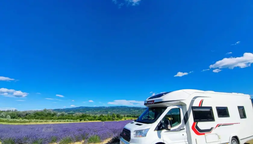Un camping-car blanc stationné devant un champ de lavande en fleur, sous un ciel bleu éclatant en Provence.