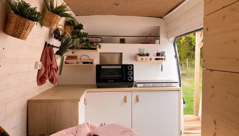 Aménagement intérieur d'un van aménagé : cuisine fonctionnelle avec four, plaque de cuisson, rangements et touches végétales.
