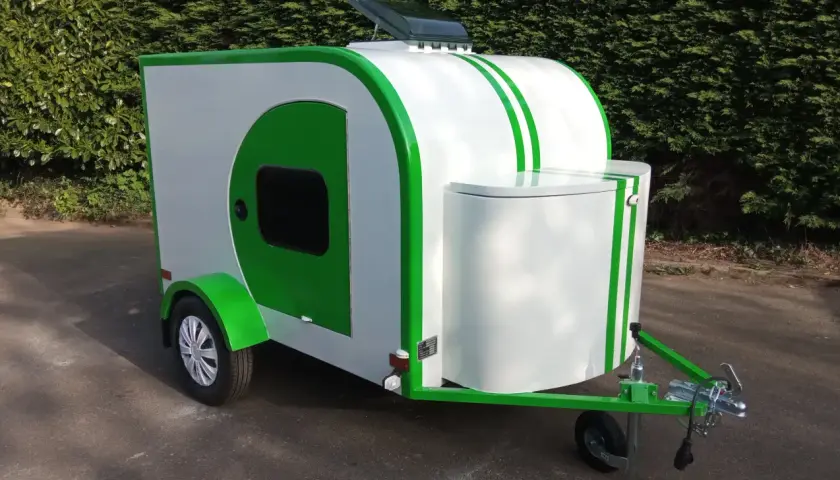 Caravane blanche et verte au design unique, rappelant une goutte d'eau. Parfaite pour des escapades écologiques.