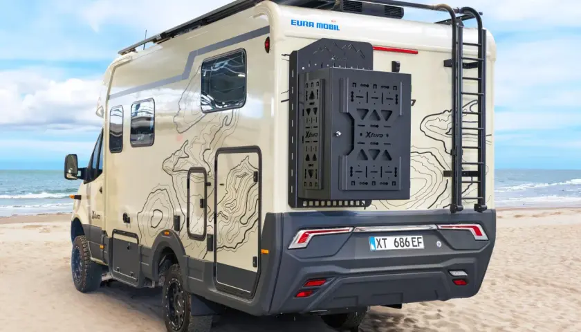 Camping-car Eura Mobil Xtura sur une plage de sable, avec une échelle arrière et un porte-roue noir.