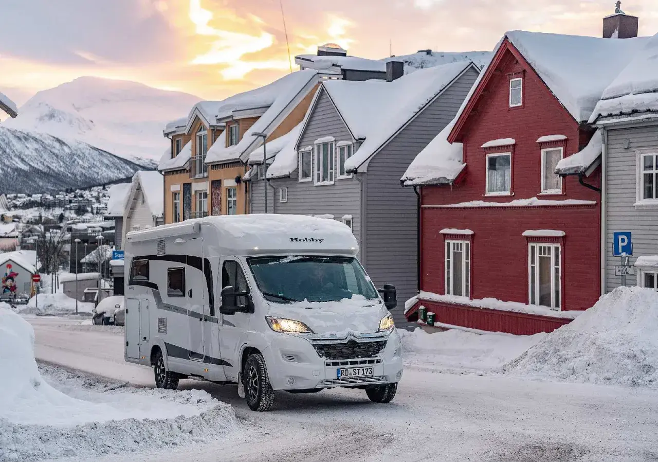 Un camping-car blanc roule dans une rue enneigée. Il semble être le camping-car le mieux isolé pour affronter le froid.