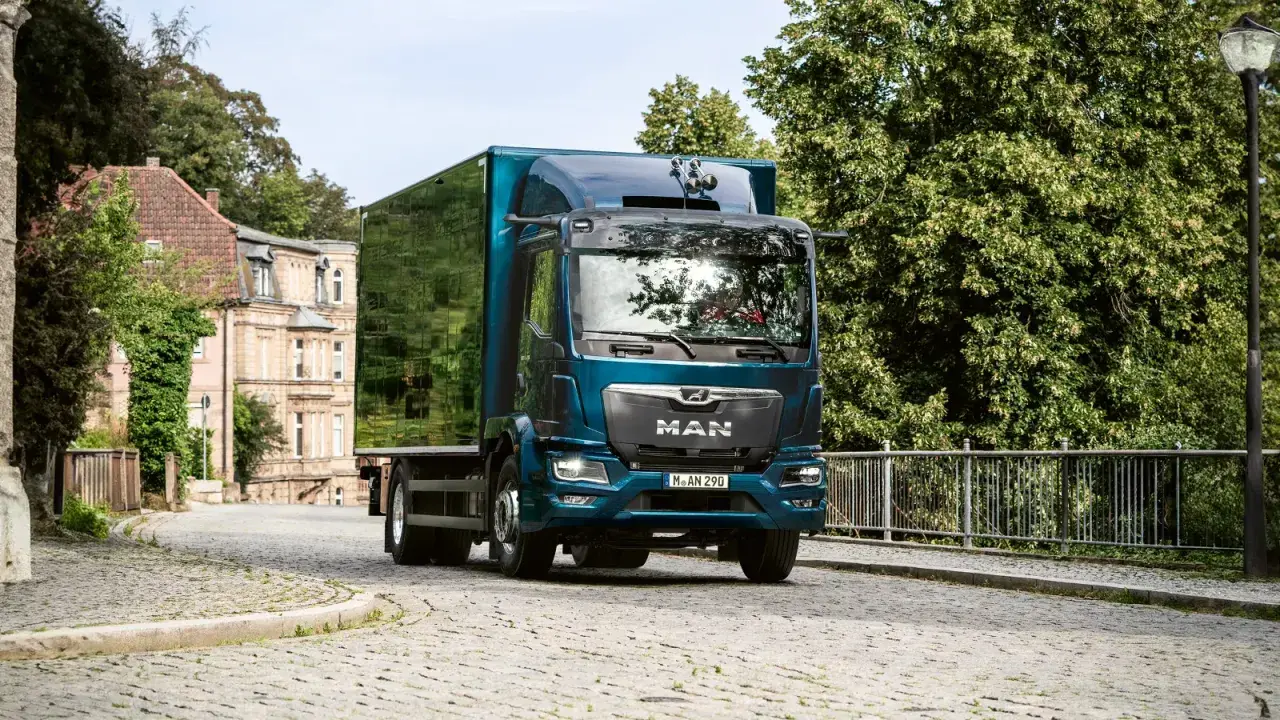 Camion MAN bleu turquoise avec remorque verte sur une route pavée.