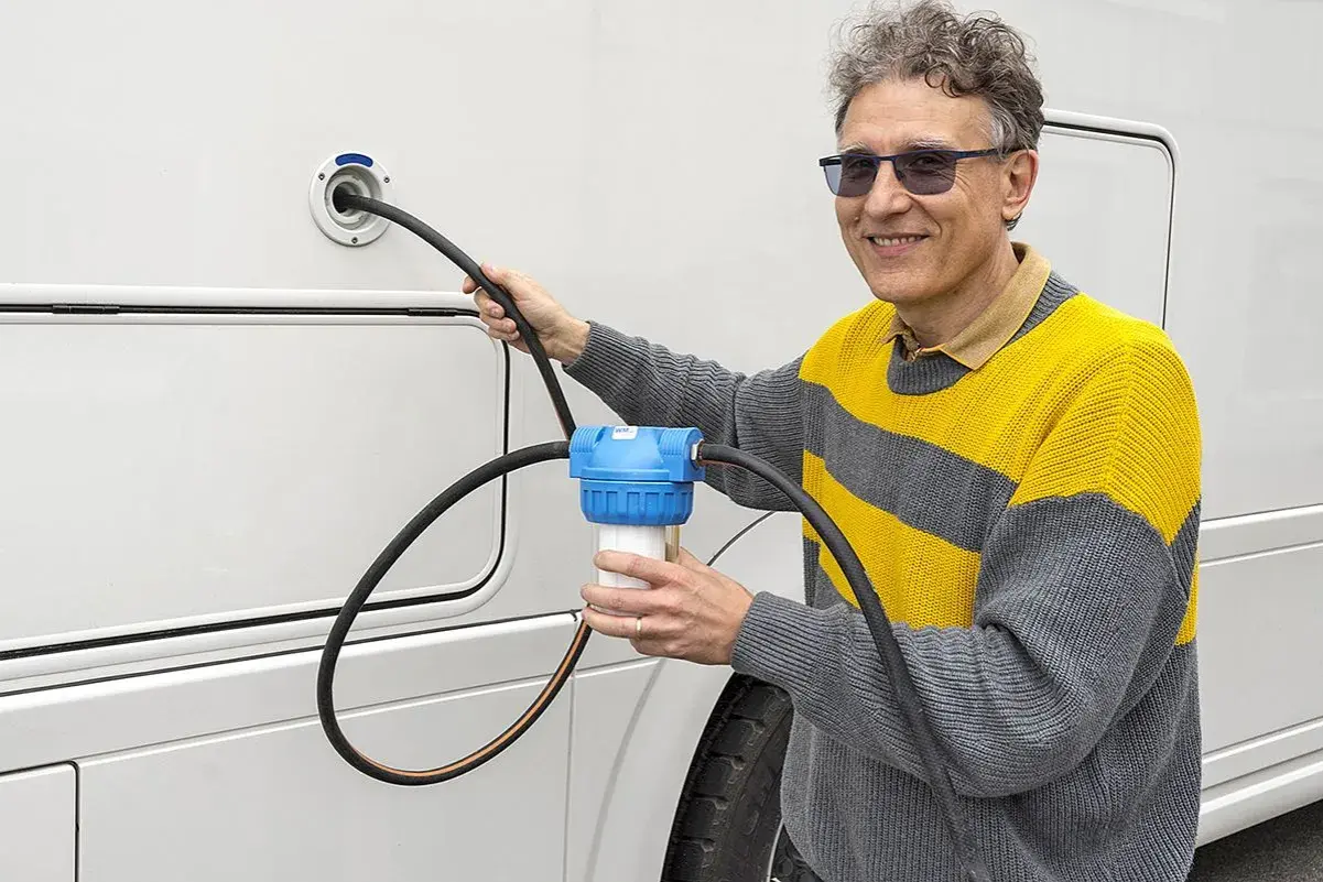 Un homme utilise un filtre à eau pour le remplissage d'eau de son camping-car. Une astuce pratique pour une eau pure en voyage.