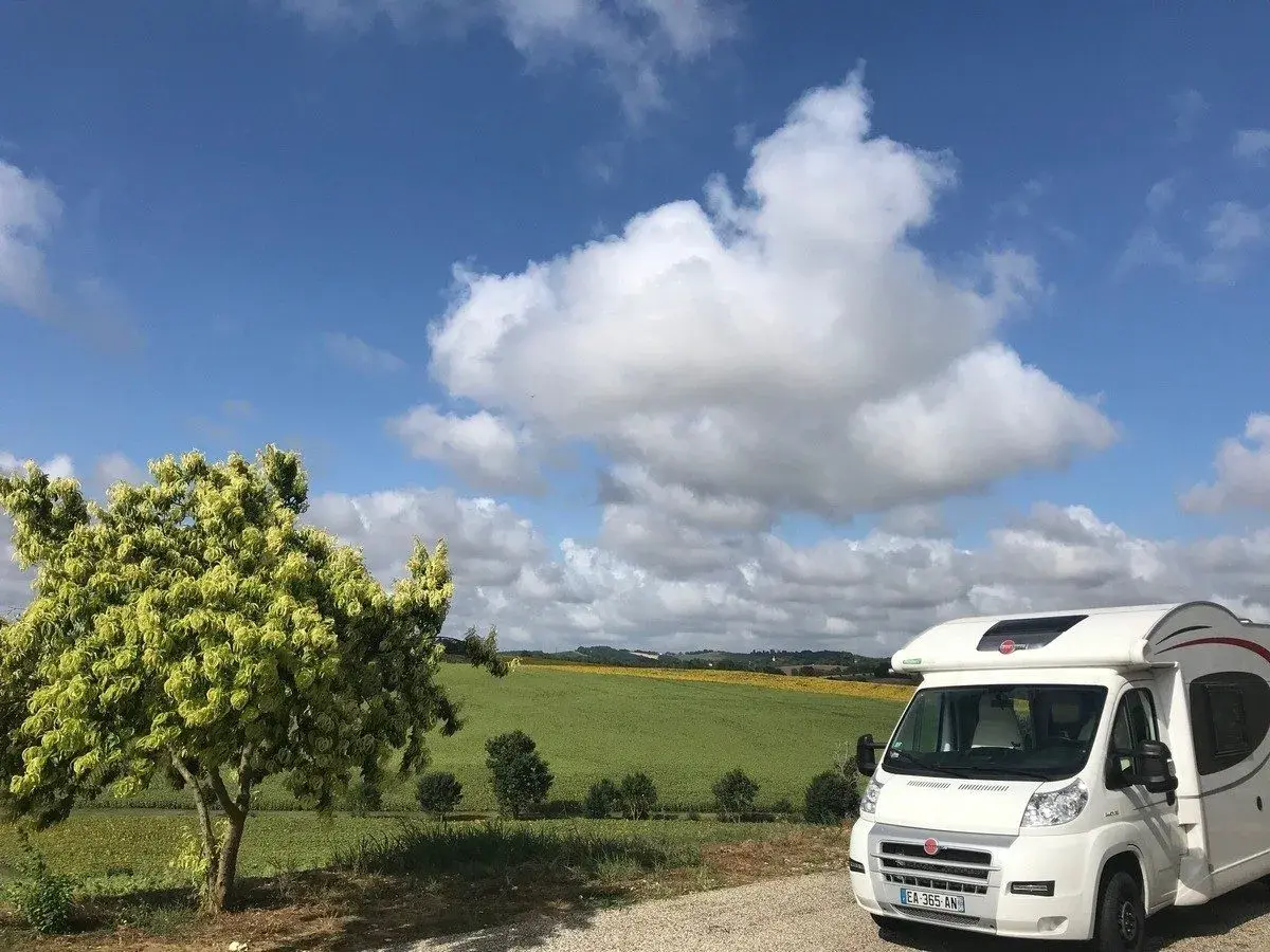 Camping-car en France, sous un ciel bleu et nuageux, avec un champ de tournesols en arrière-plan. La passion du voyage en camping-car.