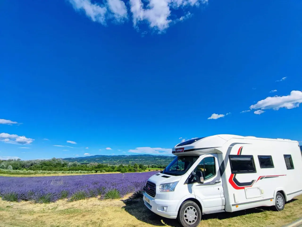 Un camping-car blanc stationné devant un champ de lavande en fleur, sous un ciel bleu éclatant en Provence.