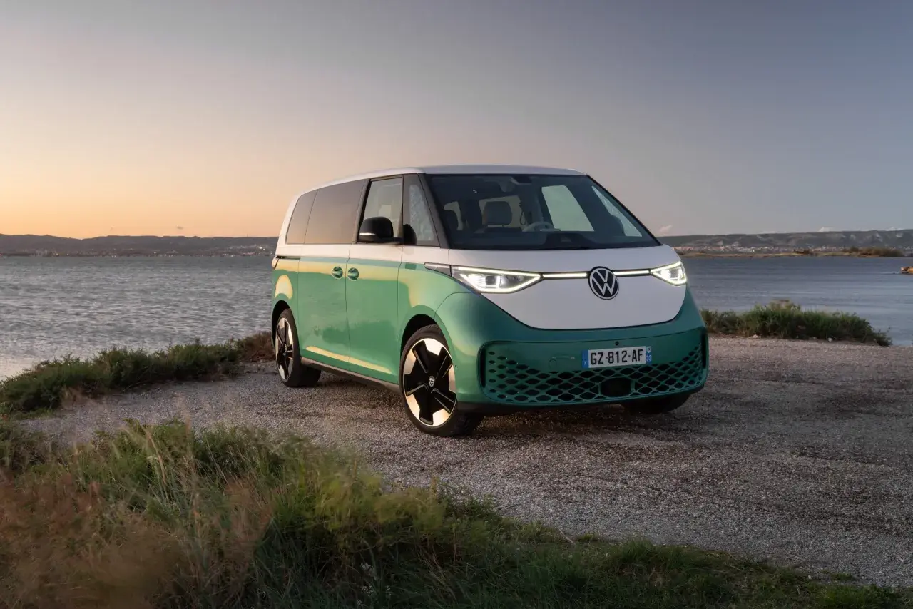 Un camping-car électrique vert et blanc, prêt pour l'aventure au bord de l'eau au coucher du soleil.