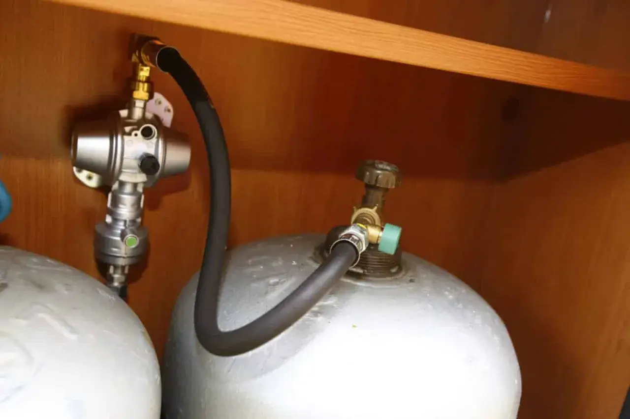 Connexion pour remplir bouteille de gaz au GPL. Tuyau noir relié à une valve verte sur la bouteille.