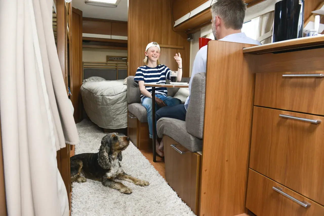 Un enfant et un homme discutent dans un camping-car, un chien au sol. Une astuce chauffage camping-car pour un voyage confortable.