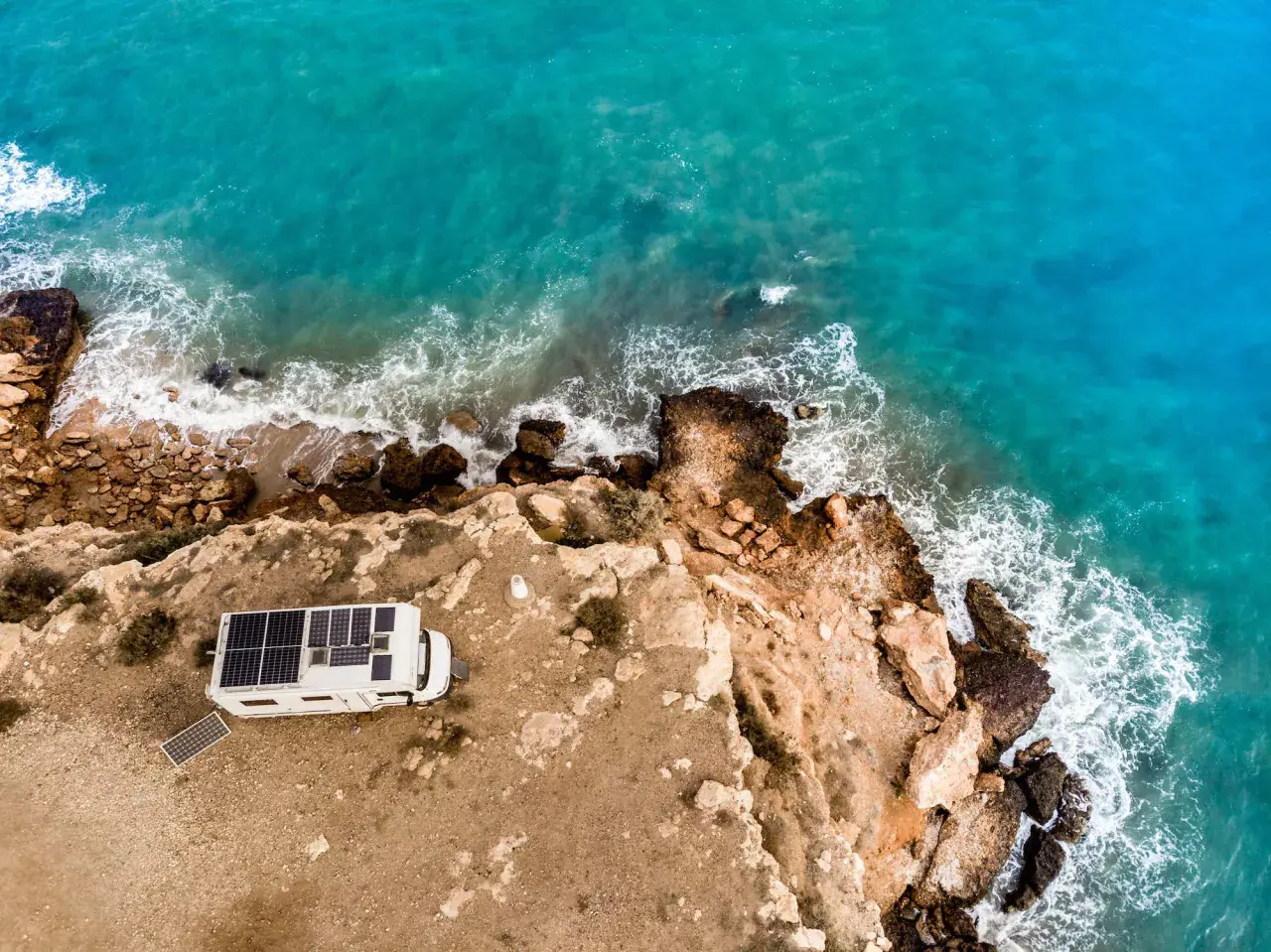 Camping-car avec panneaux solaires sur une falaise en Espagne, face à la mer turquoise. Une belle escapade de camping chez l'habitant.