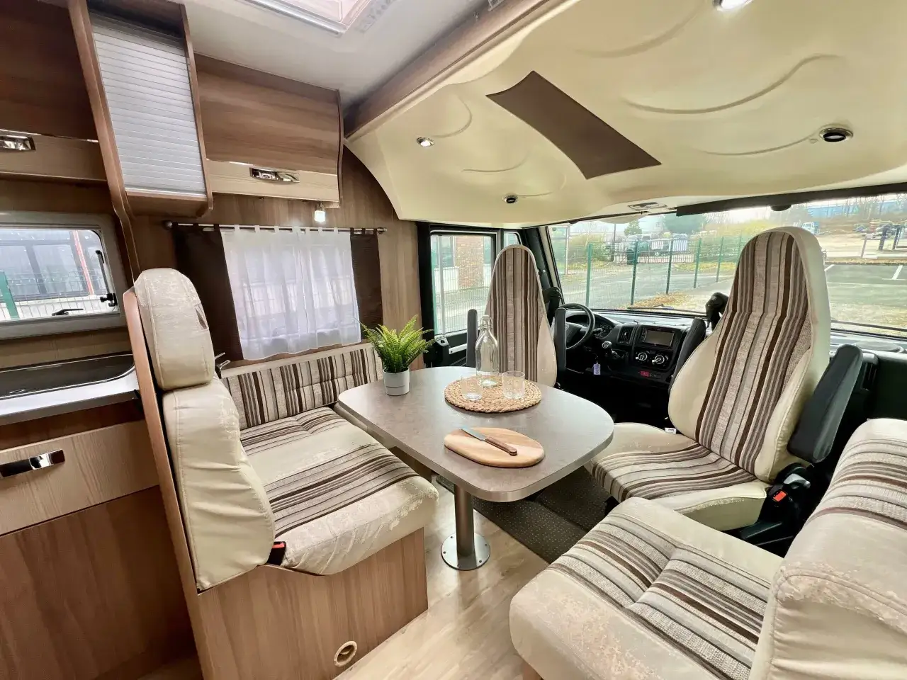 Intérieur du camping-car Pilote G740 : salon avec banquettes, table, sièges pivotants et cuisine.