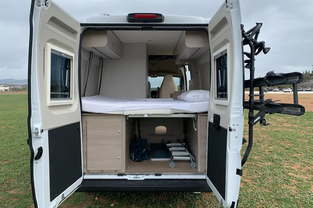 Aménagement intérieur d'un camping-car prêt pour le camping chez l'habitant en Espagne. Lit, rangements et porte-vélos visible.