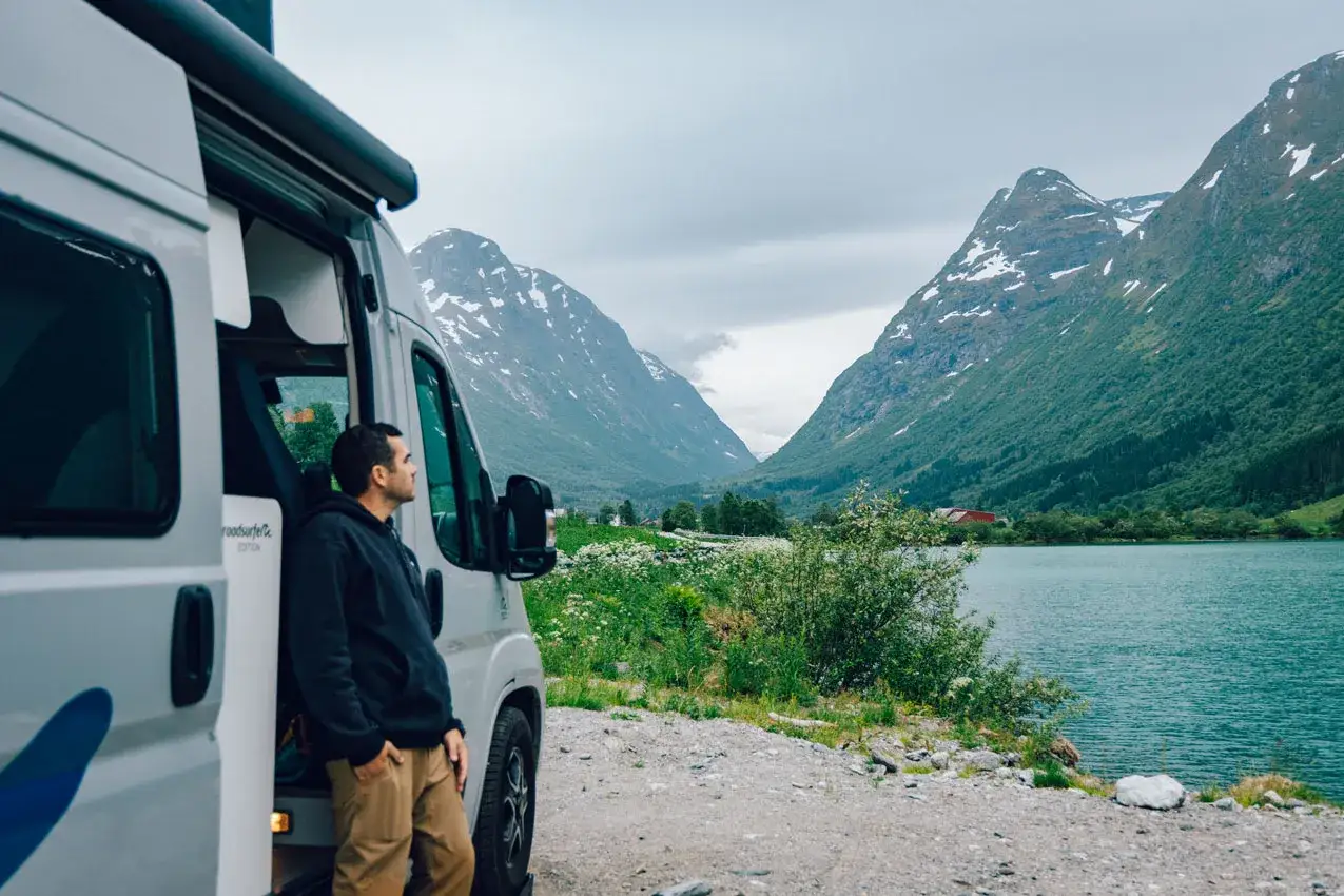 Un homme contemplant un paysage de montagne spectaculaire pr&egrave;s d'un lac, van am&eacute;nag&eacute;. Ce d&eacute;cor idyllique pourrait bien &ecirc;tre le meilleur pays pour voyager en van.