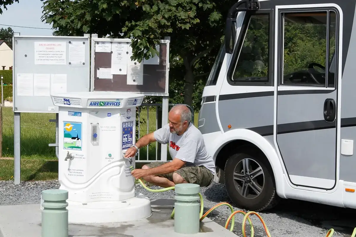 Un homme fait le plein d'eau de son camping-car &agrave; une borne de services. Une astuce remplissage eau camping-car efficace.