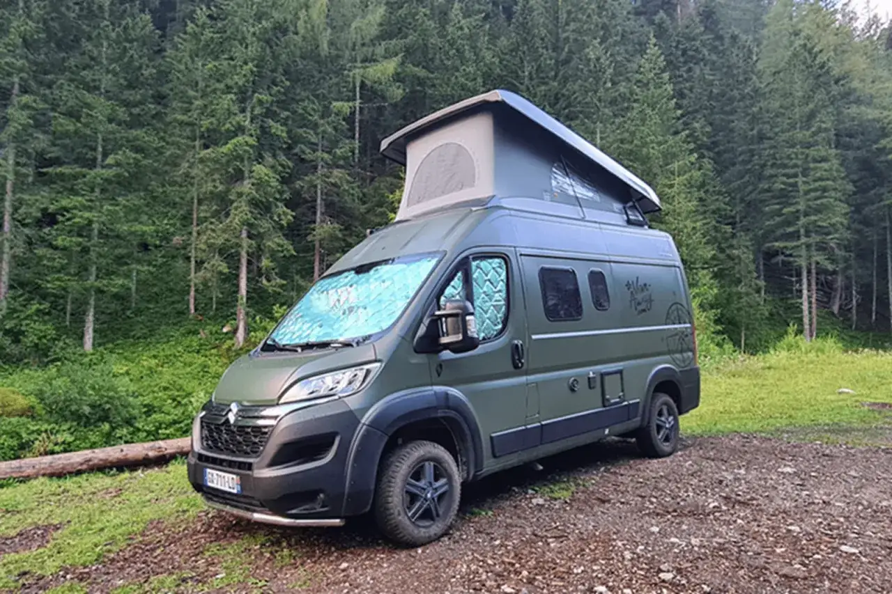 Un van tout terrain vert, prêt pour l'aventure, garé dans une forêt de pins.