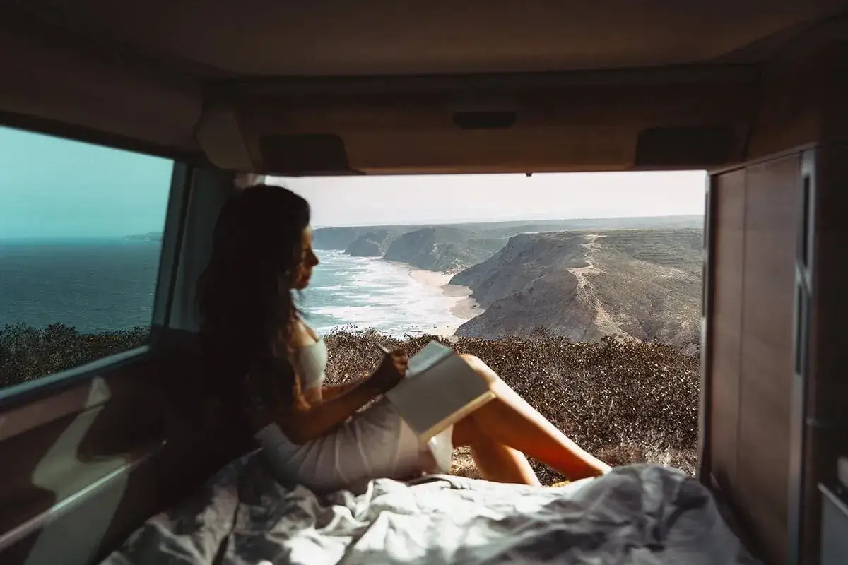 Femme lisant dans un camping-car avec vue sur la c&ocirc;te portugaise. Id&eacute;al pour planifier son budget pour aller au Portugal en camping-car.