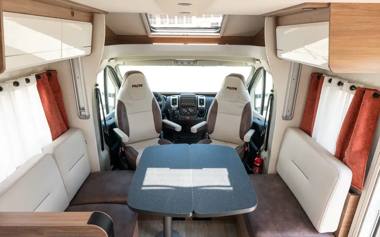 Intérieur d'un camping-car Pilote P 726 FC. Avis sur ce modèle : sièges confortables, table modulable, ambiance cosy.