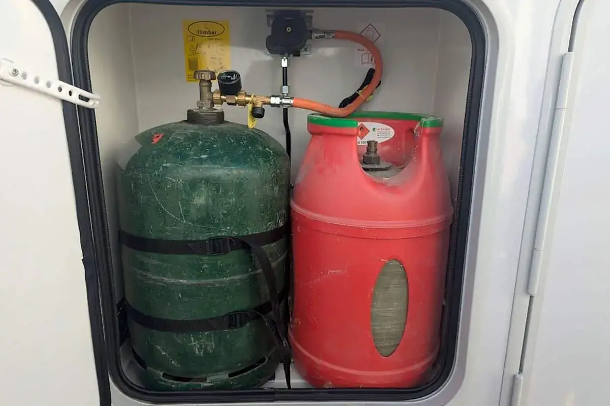Deux bouteilles de gaz (verte et rouge) dans un compartiment de camping-car, assurant l'autonomie en gaz pour le voyage.